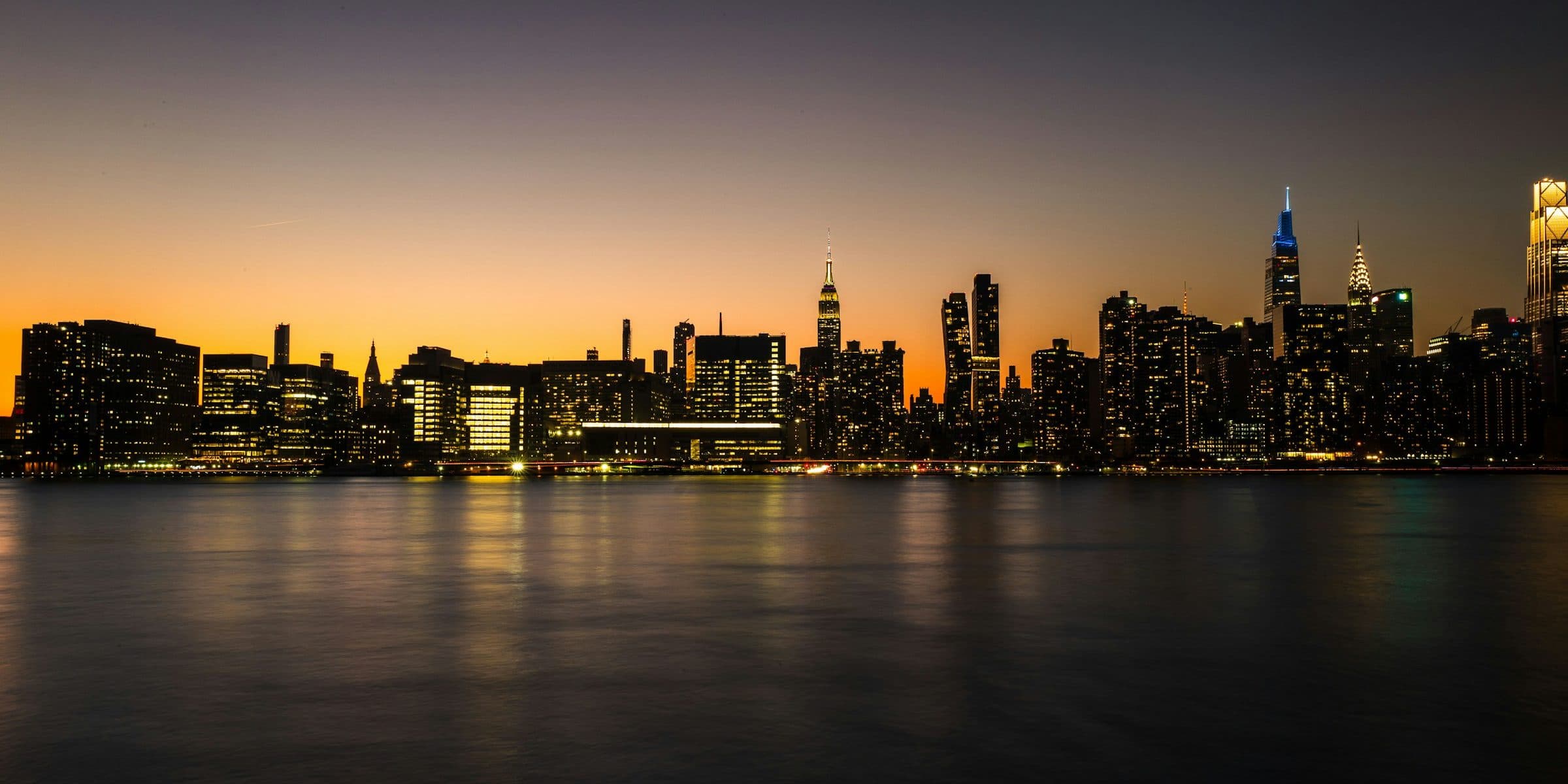 The Midtown Manhattan skyline at dusk seen across the East River, office windows lit